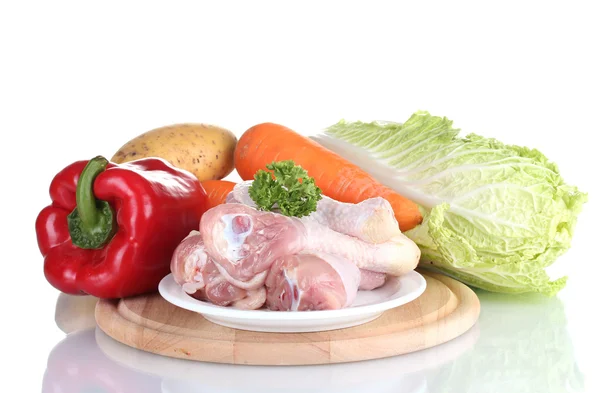 Fresh vegetables with raw chicken drumsticks on cutting board isolated on white — Stock Photo, Image