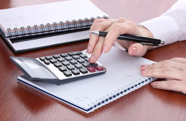 Ręce kobiety z ołówkiem, notebooki i kalkulator na drewnianym stole — Zdjęcie stockowe