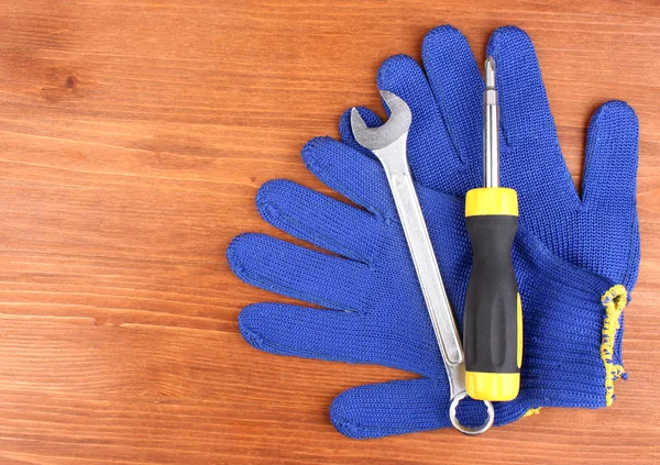 Klíč a šroubovák s rukavicemi na dřevěné pozadí — Stock fotografie