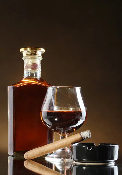 Fles en glas brandy en sigaar op bruine achtergrond — Stockfoto