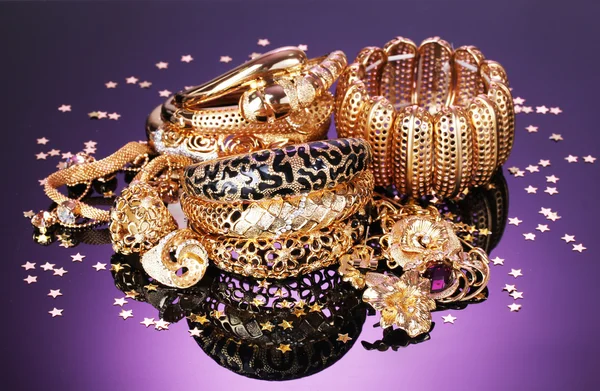 Beautiful golden jewelry on purple background — Stock Photo, Image