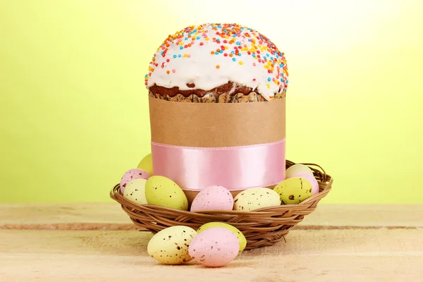 Vackra påsk kaka i korg med ägg på träbord på grön bakgrund — Stockfoto