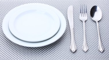 White empty plates with fork, spoon and knife on a grey tablecloth