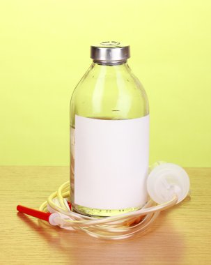 Bottle of intravenous antibiotics and plastic infusion set on wooden table on green background clipart