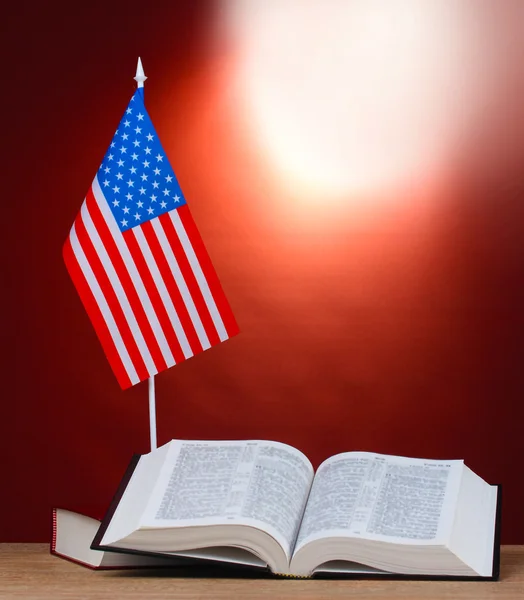 Bandeira americana no estande e livros sobre mesa de madeira no fundo vermelho — Fotografia de Stock