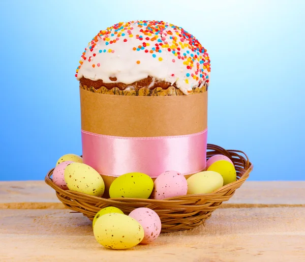 Beautiful Easter cake in basket with eggs on wooden table on blue background — Stockfoto