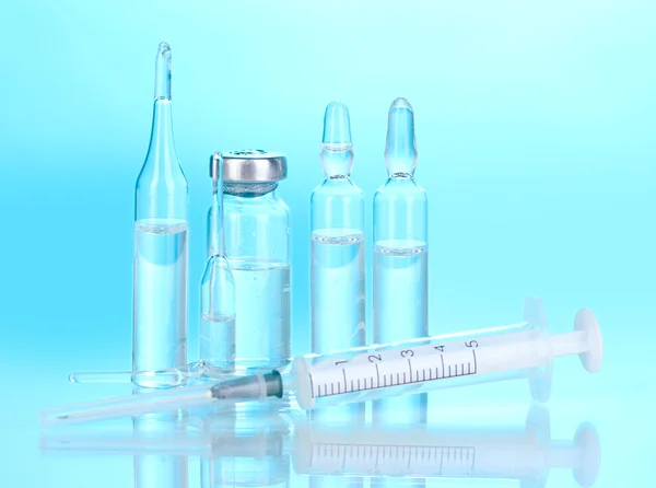 Spritze und medizinische Ampullen auf blauem Hintergrund — Stockfoto