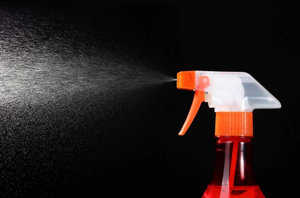 Spray bottle and spraying on black background — Stock Photo, Image
