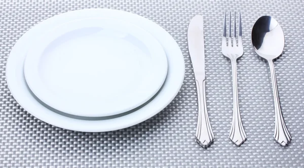 Platos blancos vacíos con tenedor, cuchara y cuchillo sobre un mantel gris — Foto de Stock