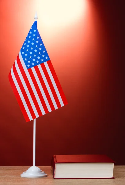 American flag on the stand and book on wooden table on red background — Stock Photo, Image