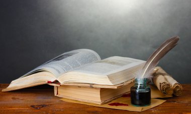 Old books, scrolls, feather pen and inkwell on wooden table on grey background clipart