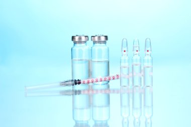 Syringe and medical ampoules on blue background clipart