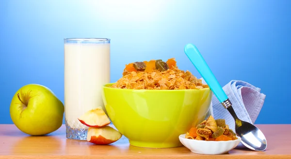Sabrosos copos de maíz en tazón verde, manzanas y vaso de leche sobre mesa de madera sobre fondo azul — Foto de Stock