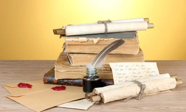 Libros antiguos, pergaminos, plumas y tintero sobre mesa de madera sobre fondo amarillo —  Fotos de Stock
