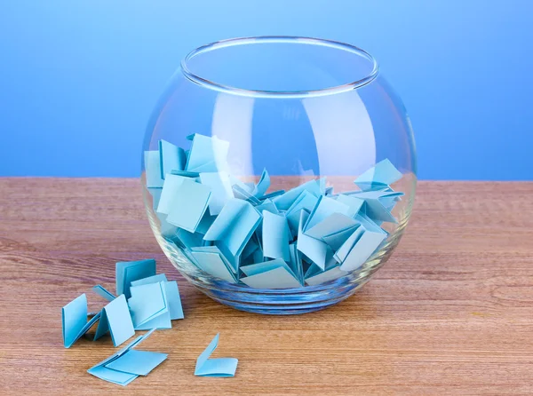 Papierschnipsel für Lotterie in Vase auf Holztisch auf blauem Hintergrund — Stockfoto
