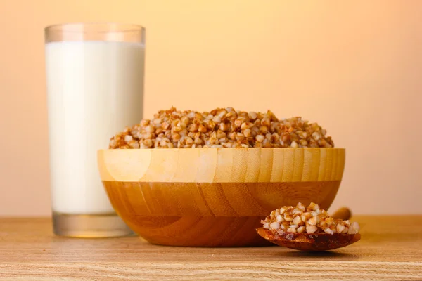 Boiled buckwheat in a wooden bowl with a glass of milk on wooden table on brown — Stock Photo, Image