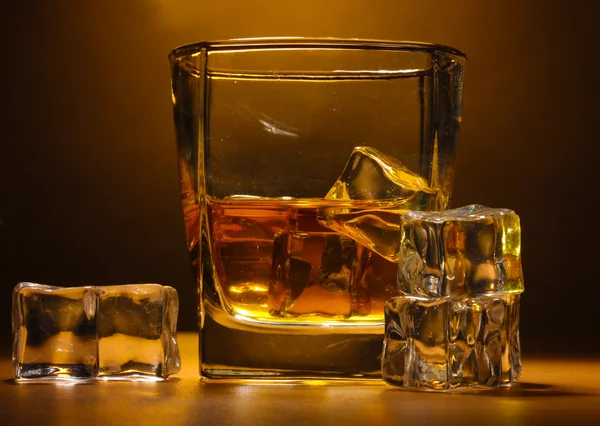 スコッチ ウイスキーと茶色の背景に木製のテーブルの上の氷のグラス — ストック写真