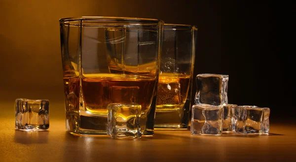 Due bicchieri di whisky scozzese e ghiaccio sul tavolo di legno su sfondo marrone — Foto Stock