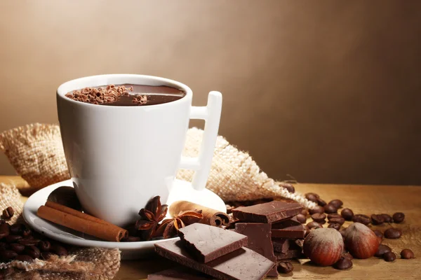Taza de chocolate caliente, palitos de canela, nueces y chocolate en la mesa de madera sobre fondo marrón —  Fotos de Stock