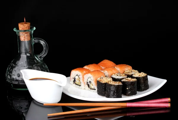 stock image Tasty rolls served on white plate with chopsticks and soy sauce isolated on black