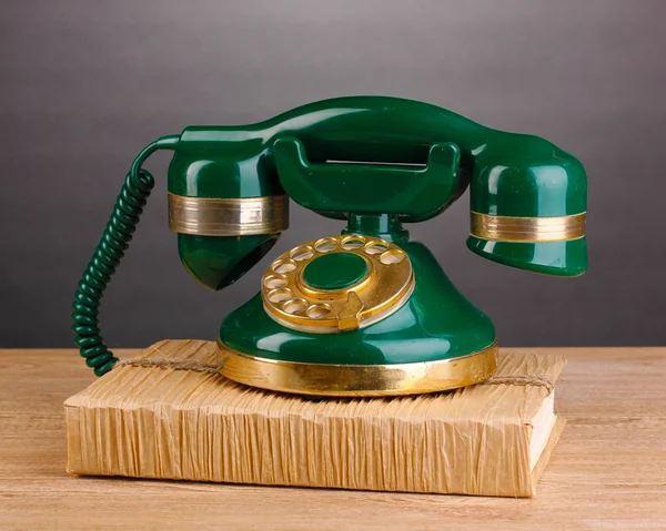 Ретро-телефон, стоящий на книге на деревянном столе на сером фоне — стоковое фото