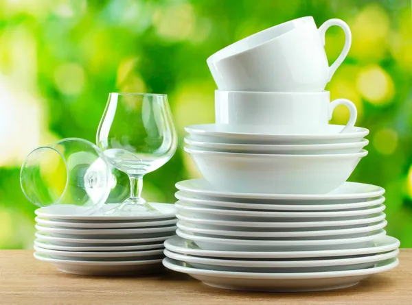 Sauberes Geschirr auf Holztisch auf grünem Hintergrund — Stockfoto