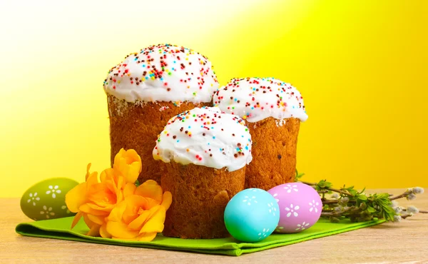 Hermosos pasteles de Pascua, huevos coloridos y ramitas de coño y sauce en la mesa de madera sobre fondo amarillo —  Fotos de Stock