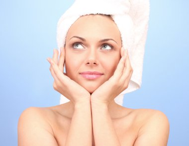 Beautiful young woman after shower with a towel on her head on blue background close-up