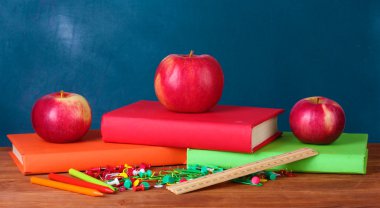 Composition of books, stationery and an apples on the teachers desk in the background of the blackboard clipart