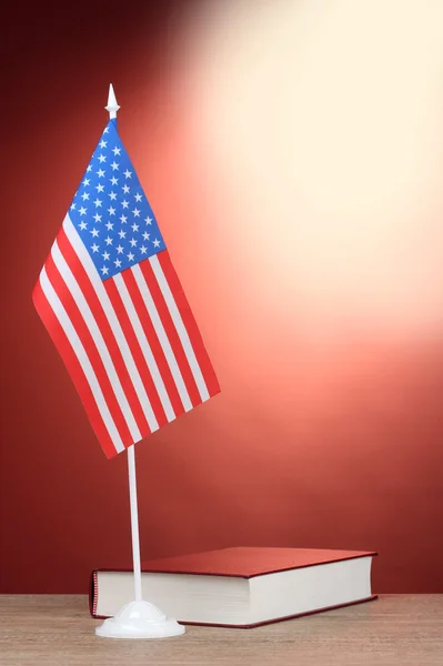 Bandera americana en el stand y libro sobre mesa de madera sobre fondo rojo —  Fotos de Stock