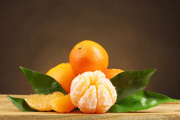 Mandarino con foglie su tavolo di legno su sfondo marrone — Foto Stock