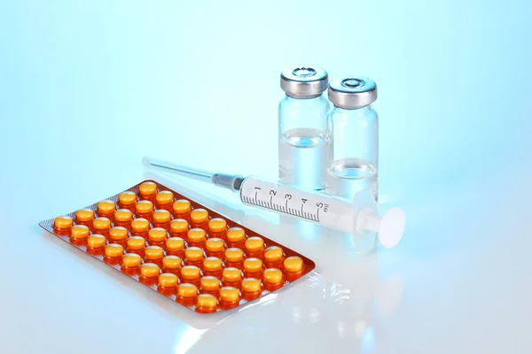 Stříkačka s lékařskou ampulí a tablety na modrém pozadí — Stock fotografie