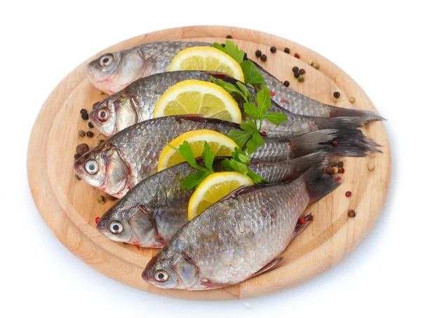Свежие рыбы с лимоном, петрушкой и специями на деревянной разделочной доске изолированы на белом — стоковое фото