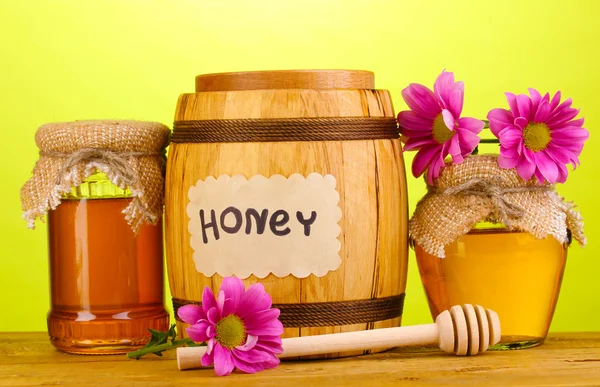 Süßer Honig in Fässern und Gläsern mit Nieselregen auf Holztisch auf grünem Hintergrund — Stockfoto
