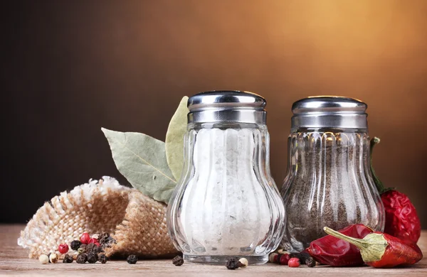 stock image Salt and pepper mills and spices on wooden table on brown background