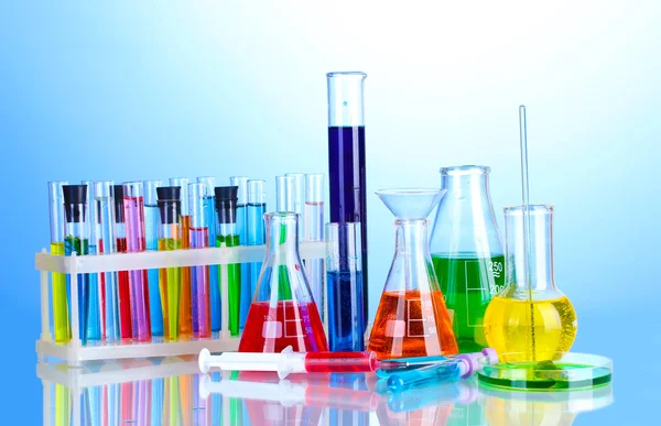 Different laboratory glassware with color liquid on blue background — Stock Photo, Image