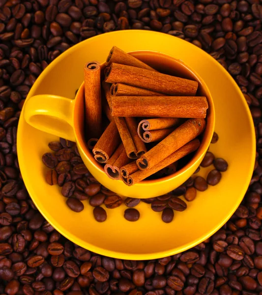 Composição da xícara amarela com grãos de café e canela close-up — Fotografia de Stock