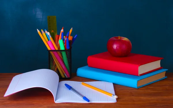 Sammansättningen av böcker, pappersvaror och en äpplen på lärare skrivbordet i bakgrunden i tavlan — Stockfoto
