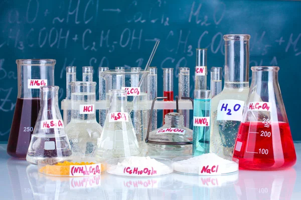 Probówki z różnych kwasów i innych środków chemicznych na tle tablicy — Zdjęcie stockowe