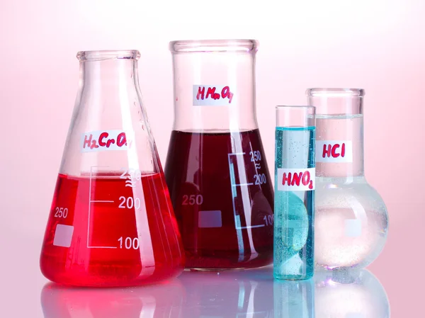 Пробирки с различными кислотами и химикатами на розовом фоне — стоковое фото