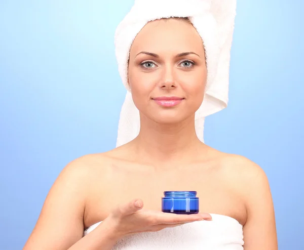 Красивая молодая женщина после душа с полотенцем на голове и банка сливок в руке на синем фоне крупным планом — стоковое фото