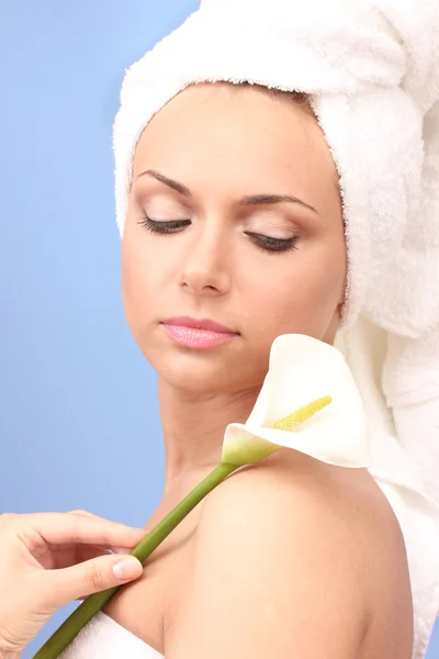 Beautiful young woman after shower with a towel on her head and white calla on blue background close-up — Stock Photo, Image