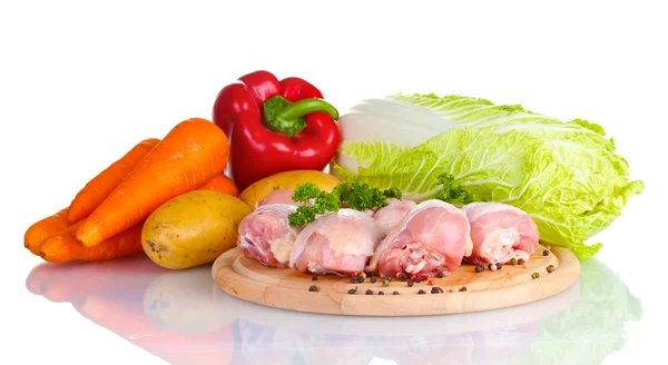 Fresh vegetables with raw chicken drumsticks and pork steak on cutting board isolated on white Royalty Free Stock Photos