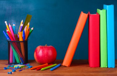 Composition of books, stationery and an apple on the teachers desk in the background of the blackboard clipart
