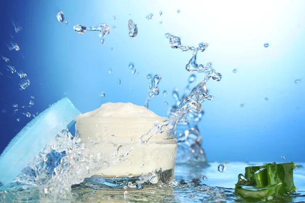 Tarro abierto de crema en salpicaduras de agua sobre fondo azul — Foto de Stock