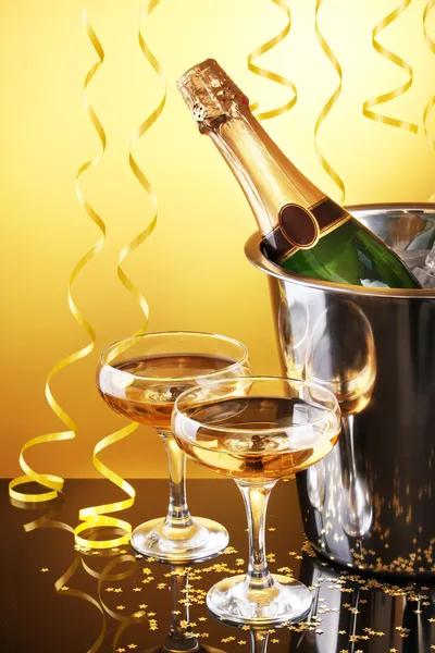 Garrafa de champanhe em balde com gelo e taças de champanhe, sobre fundo amarelo — Fotografia de Stock