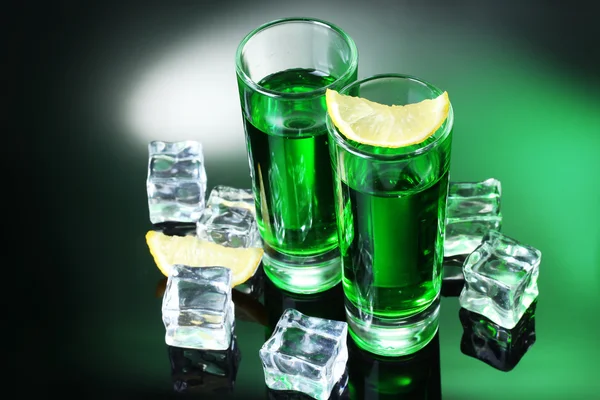 Two glasses of absinthe, lemon and ice on green background — Stock Photo, Image