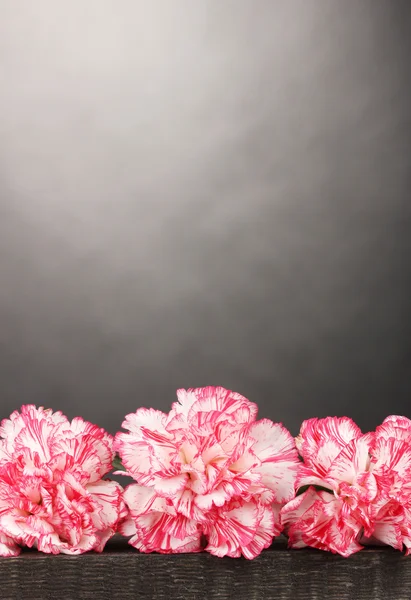 Schöne Nelken auf Holztisch auf grauem Hintergrund — Stockfoto