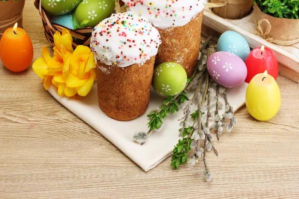Красиві великодні торти, барвисті яйця в кошику і свічки на дерев'яному столі — стокове фото