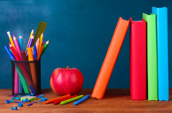 Состав книг, канцелярских принадлежностей и яблока на учительском столе на фоне доски — стоковое фото